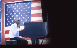 Ray Charles playing the piano with American flag in the background