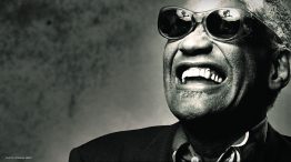 Ray Charles smiling in a collared shirt and sports jacket wearing his trademark sunglasses. PHOTO: NORMAN SEEFF